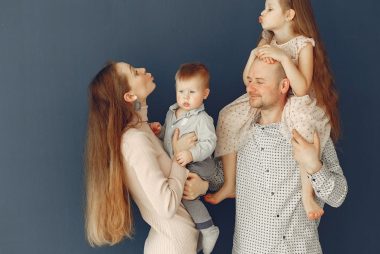 Portrait of a joyful family with parents and kids showing love and affection against a blue background.